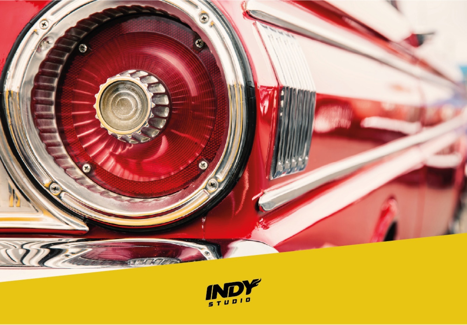 Foto macro do farol traseiro redondo e vermelho de um carro clássico, com aros cromados e a lataria vermelha brilhante.Faixa amarela na base com logotipo Indy Studio.